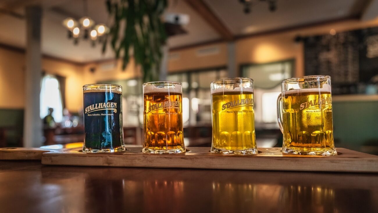 ein blaues, ein orangenes und zwei gelbe Biere aufgereiht auf einem Tresen