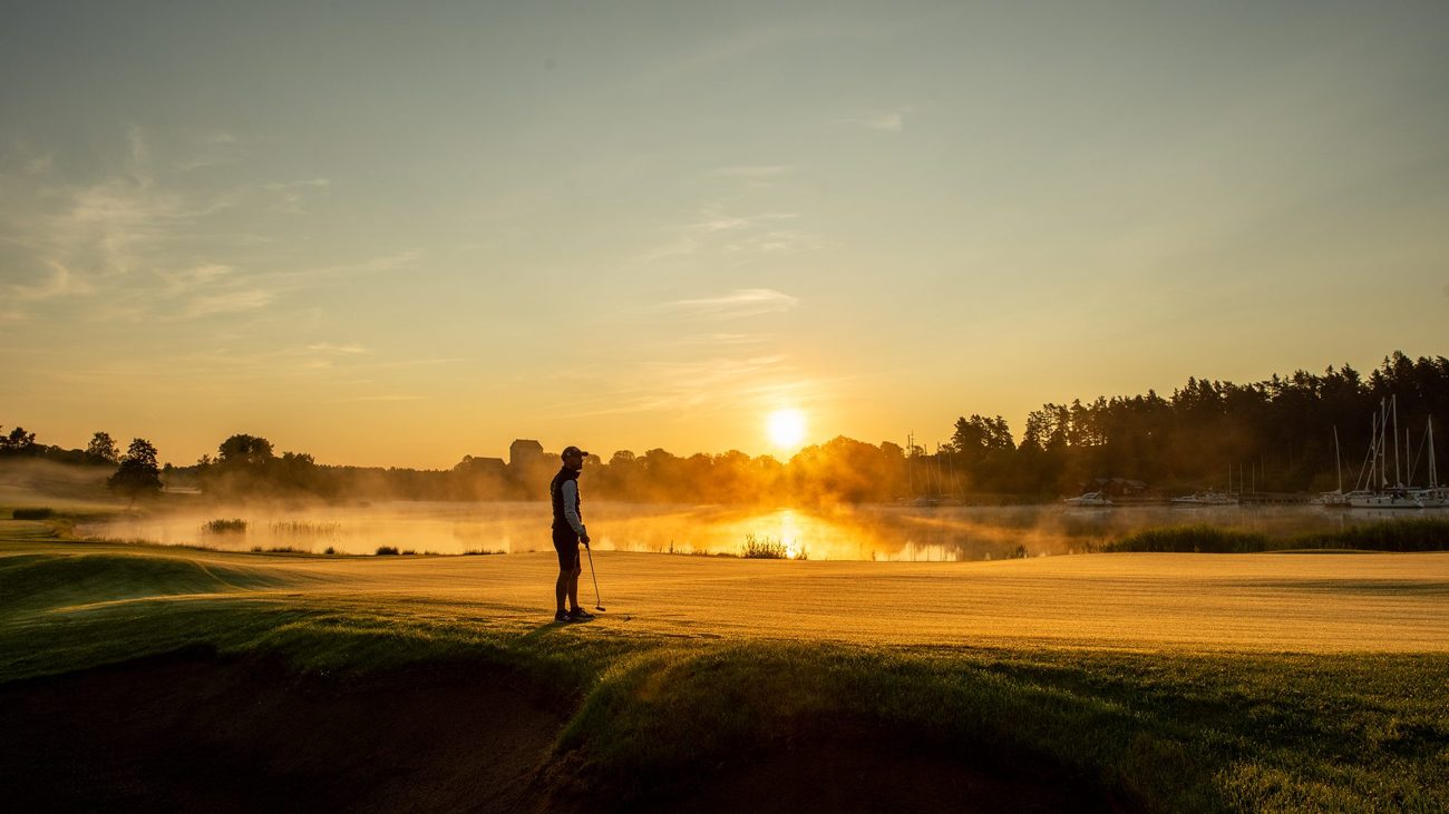 Golfer auf grüner Wiese vor der orangenen, untergehenden Sonne