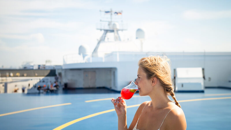 Bild på en kvinna ombord på Finnlines fartyg som dricker en drink i sommarsolen.