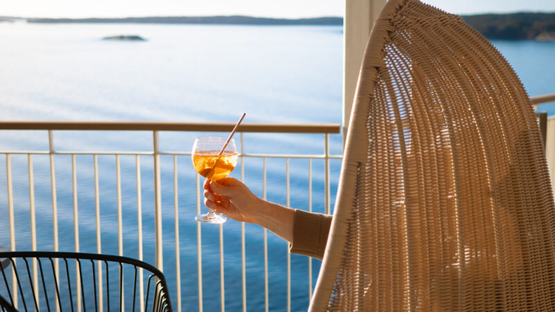 Hand som håller i en drink på däck med skärgården som utsikt