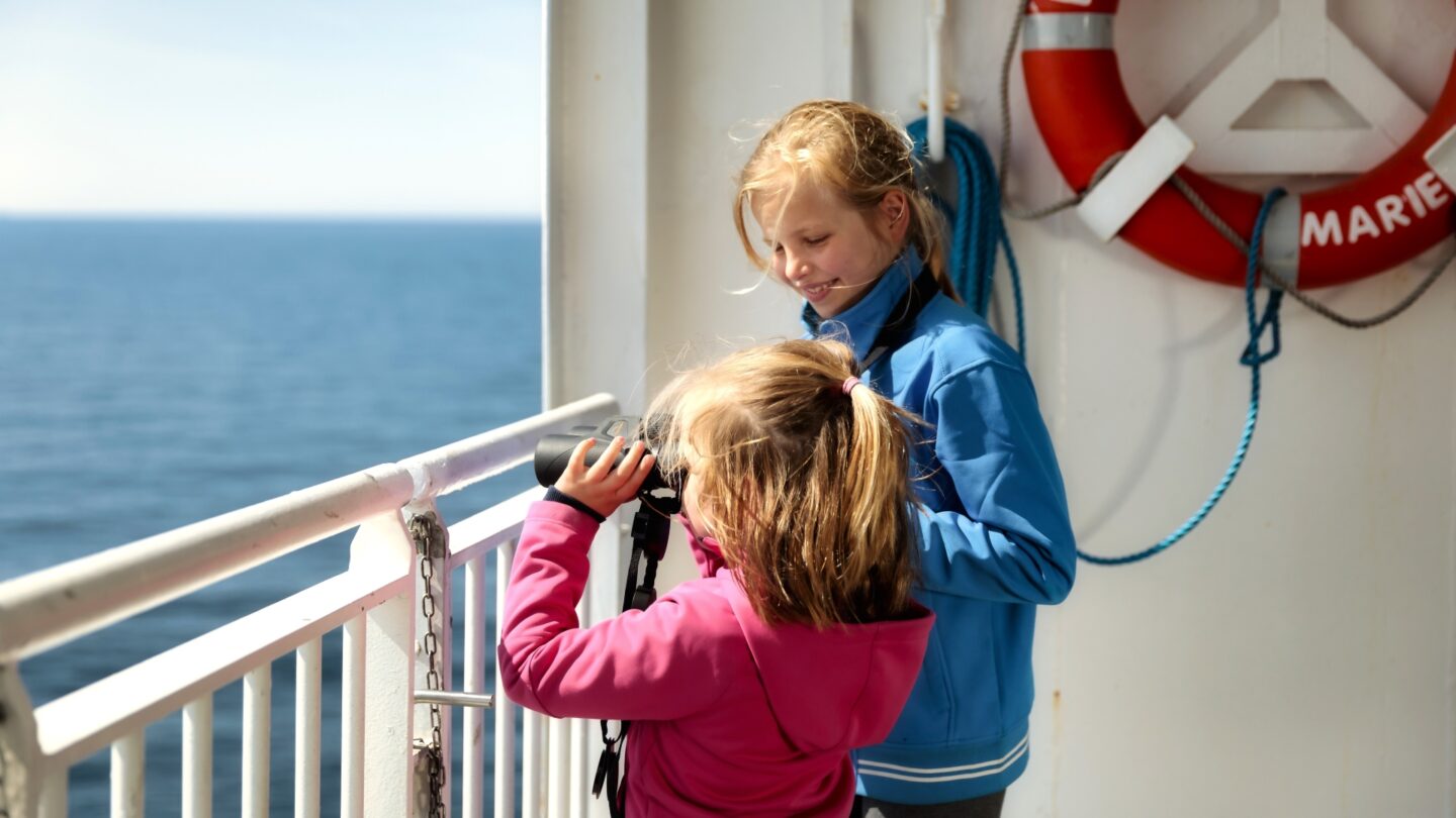 Kinder an Bord einer Fähre schauen durch ein Fernglas