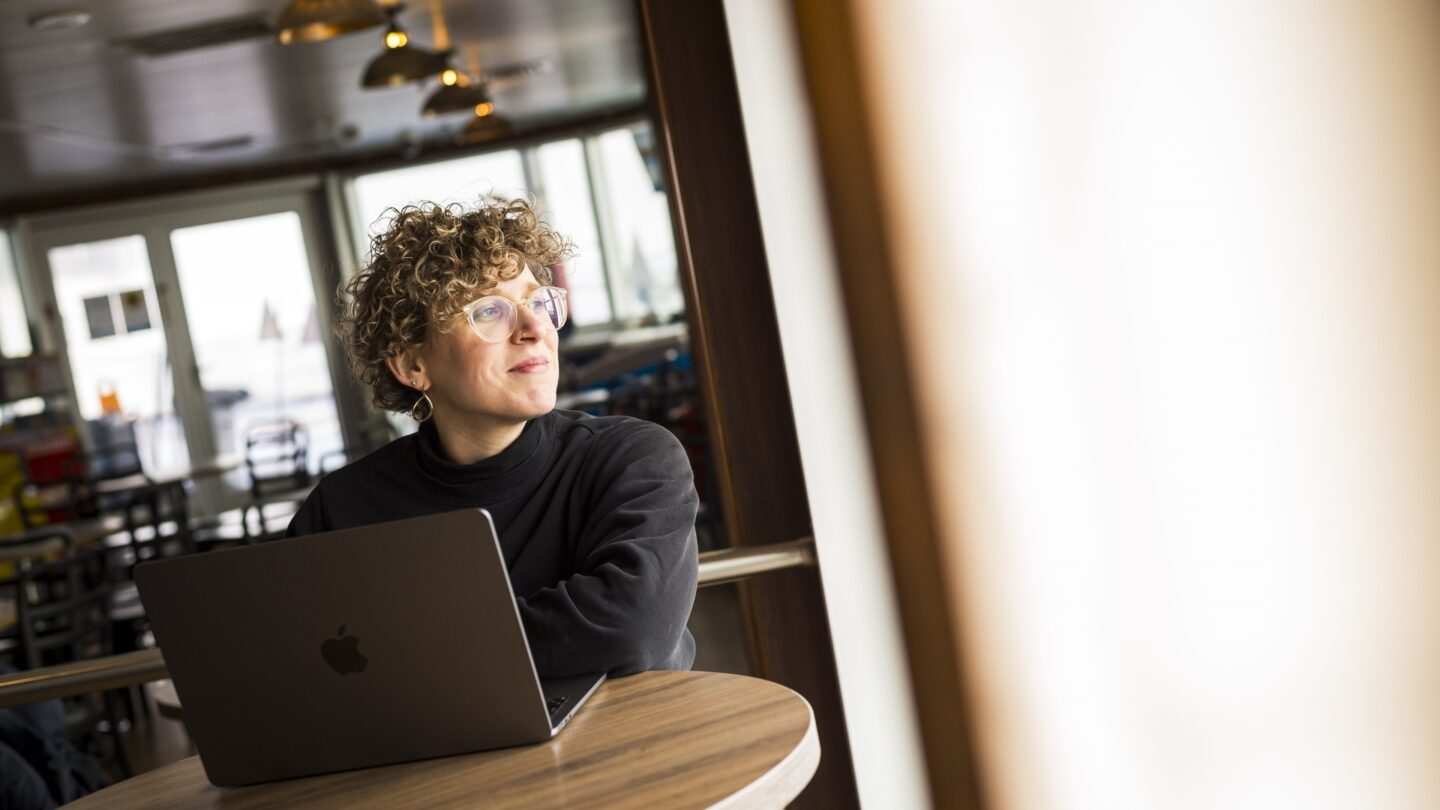 Frau mit Laptop blickt aus Fenster.