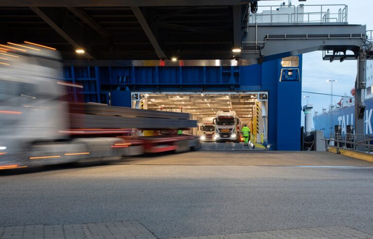 Port scene showing trucks moving on and off a cargo ship, illustrating digital transformation in port operations.