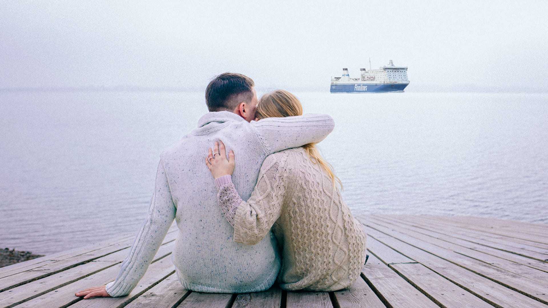 Ein Paar sitzt am Steg und blickt auf eine Finnlines-Fähre. 