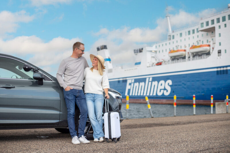 Bild på ett par som står vid sin bil framför Finnlines färja, redo för sommarsemestern.