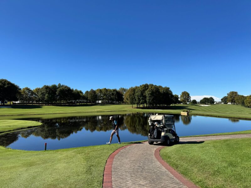 Bild på en golfare som går från sin golfbil och längst med en damm på golfbanan.