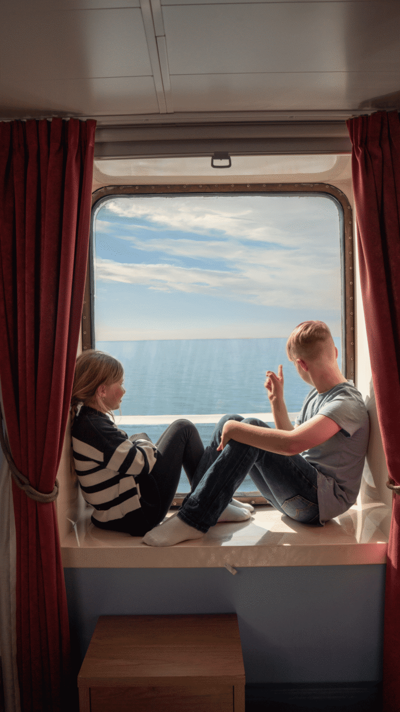 En flicka och en pojke som sitter i ett fönster ombord på Finnlines fartyg och spanar ut över havet.