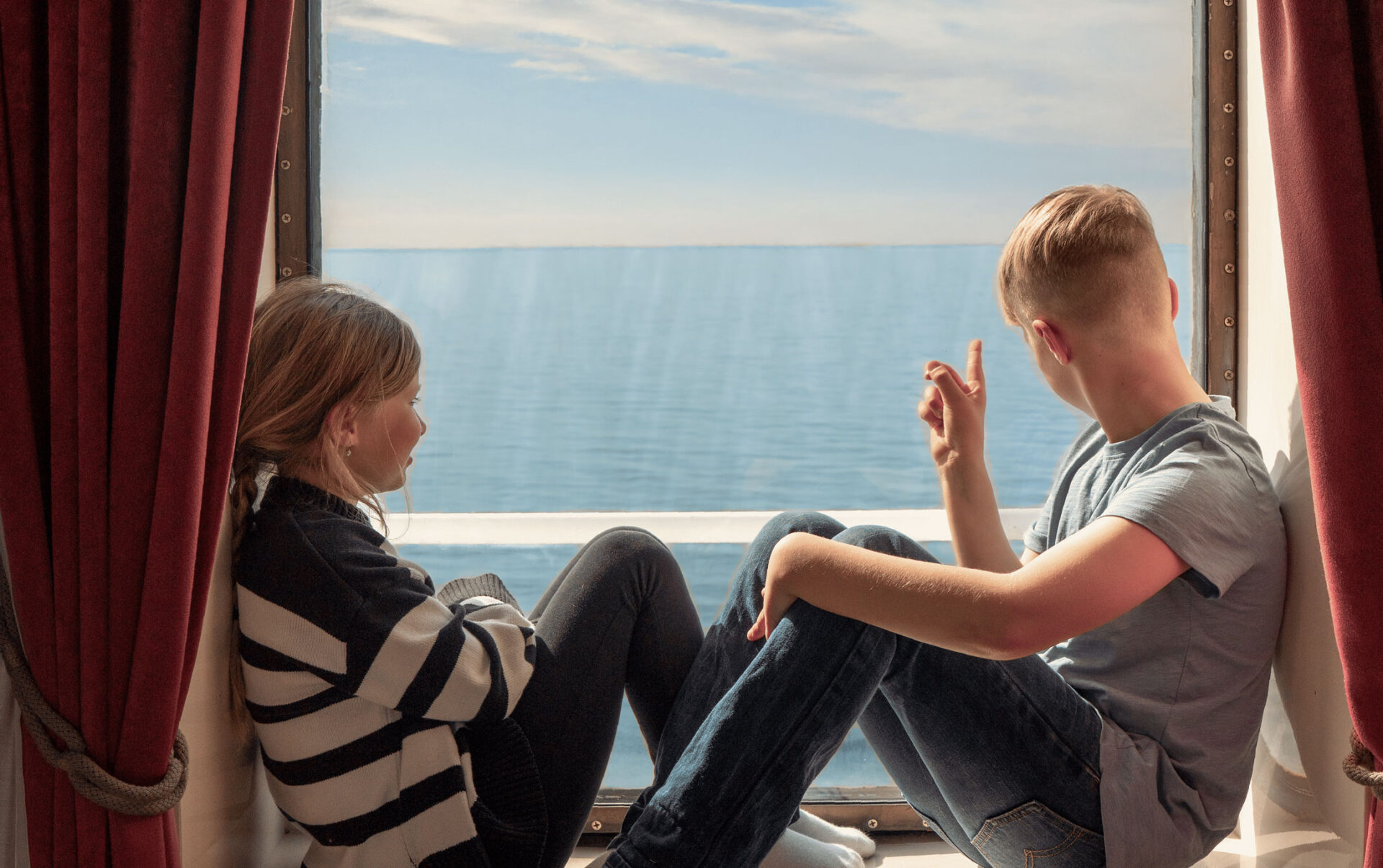 En flicka och en pojke som sitter i ett fönster ombord på Finnlines fartyg och spanar ut över havet.