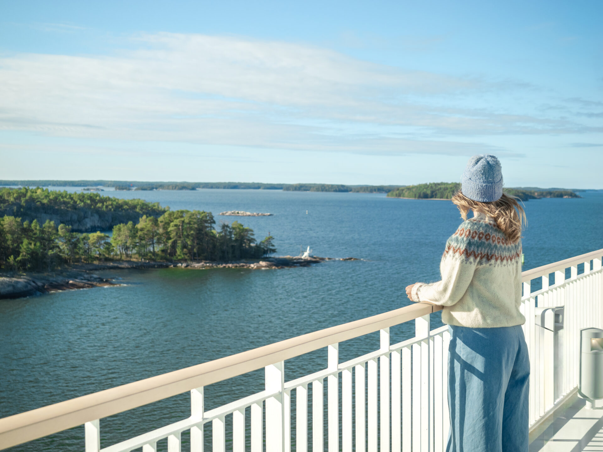 Bild på en tjej ombord på Finnlines fartyg, som står på däck och spanar ut över den finska skärgården.