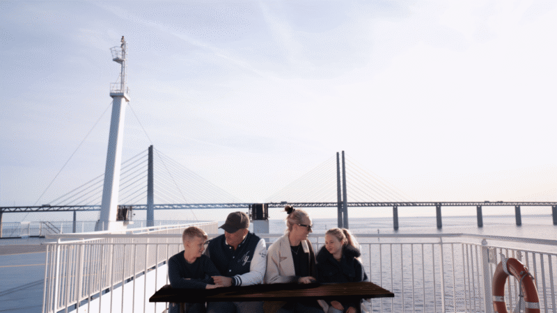 Bild på familj som sitter på däck med Öresundsbron i bakgrunden, på väg med färjan till Polen.