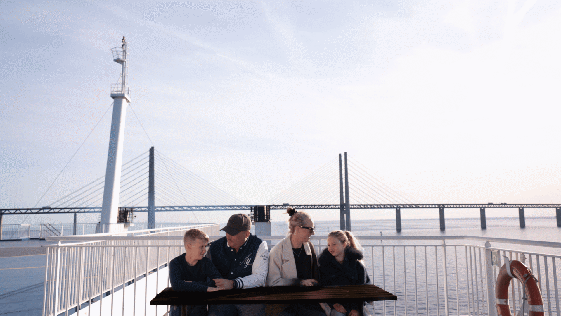 Bild på en familj med två barn som sitter på däck ombord på Finnlines fartyg, med Öresundsbron i bakgrunden. 