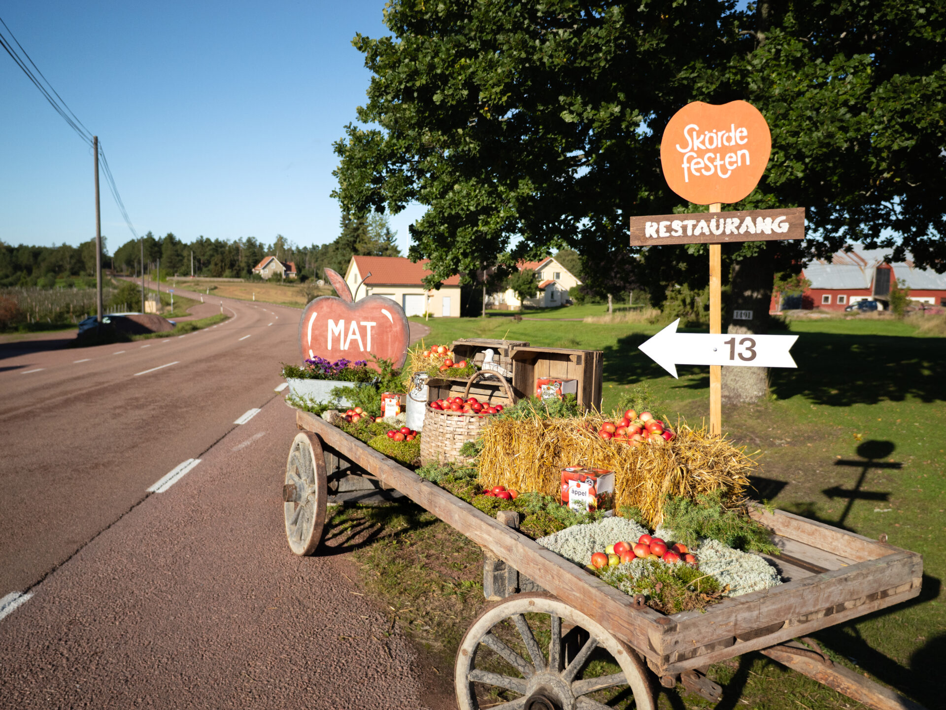 Bild på en gammal kärra fylld med äpplen och höstens färger, med skyltar som visar vägen mot Skördefesten på Åland.